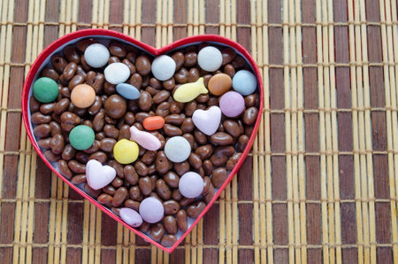 Heart shaped box filled with small chocolates balls on the wooden bamboo tableの写真素材