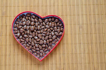 Heart shaped box filled with small chocolates balls on the wooden table