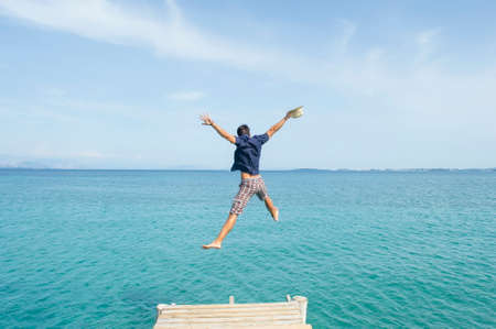 Young man jumping from the dock into the sea with his clothes onの写真素材