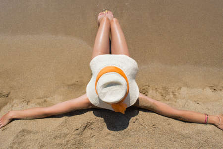 Young girl with straw hat sitting on sandy beach