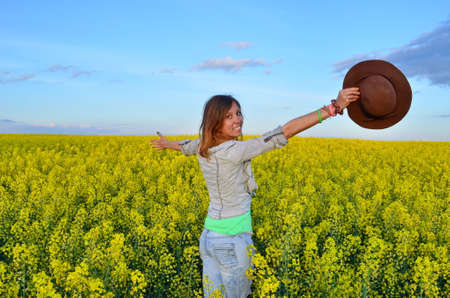 Beautiful girl posing with a hat in a field of yellow flowersの写真素材