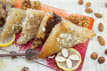 Greek baklava decorated with nuts, lemon and almonds on a decoupage table