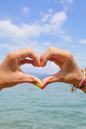 Heart shape making of hands against sea and sky looking at waterの写真素材