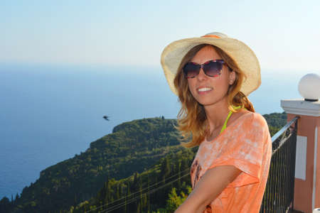 Young girl with straw hat looking at the seaside horizon from extraordinary viewpoint wearing sunglassesの写真素材