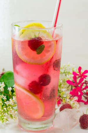 Homemade raspberry ice tea with lemon raspberry and ice cubes on a table decorated with flowersの写真素材