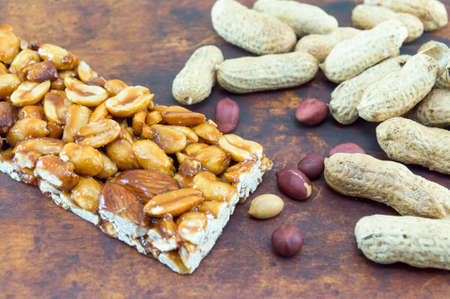 Honey bar with peanuts almonds and hazelnuts surrounded by bunch of roasted and raw peanuts placed...