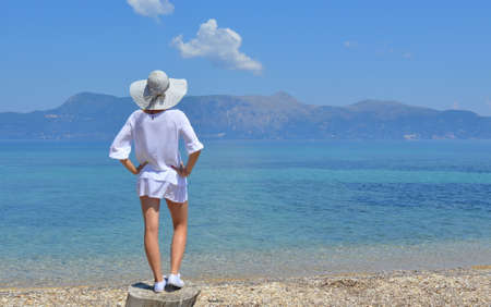 Young woman looking at the mountains above sea standing on the logの写真素材