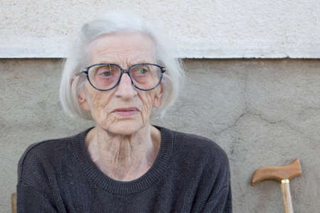 Portrait of a ninety years old grandma with walking stick sitting outdoorsの写真素材
