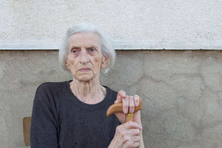 Portrait of a ninety years old grandma with walking stick sitting outdoorsの写真素材