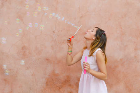 Girl blowing soap bubbles against colourful backdrop wearing pink dressの写真素材