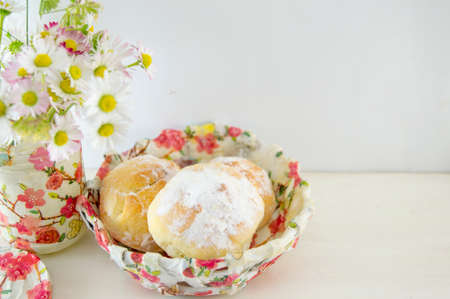 Homemade doughnuts sprinkled with powdered sugar in a decoupage decorated bowl with flowers on the tableの写真素材