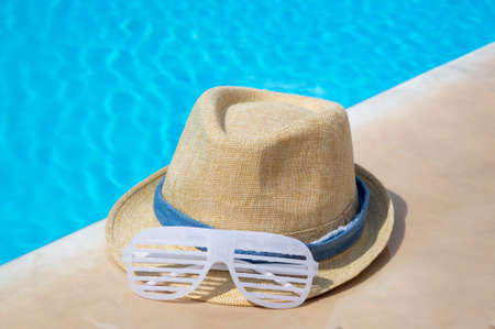 Straw hat and rave party sunglasses by the poolの写真素材