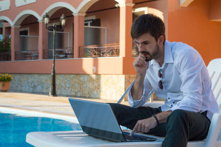 Young businessman working on his laptop by the pool while in sunbedの写真素材