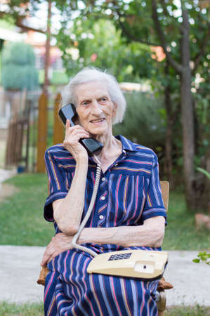Ninety years old grandma talking on a landline phone in the backyardの写真素材