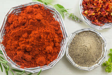 Grounded red paprika and pepper in shiny bowls on a bright wooden table close up