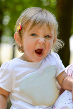Cute one year old baby girl yawning outdoors in the parkの写真素材