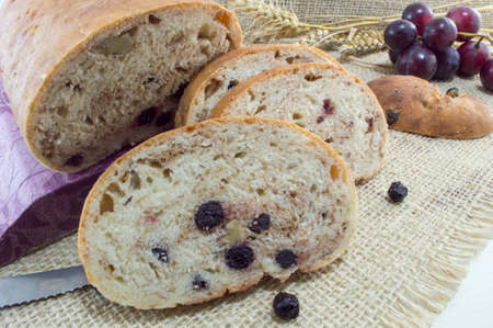 Fruit bread with aronia sliced on a wooden plate with wheat, dried aronia and fresh grape decoration