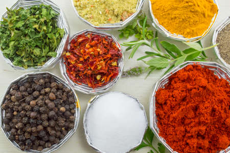 Various spices in shiny bowls with fresh plants on a white wooden table close upの写真素材