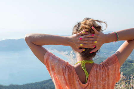 Girl with hands on her head facing the extraordinary view at the seaside from mountain viewpointの写真素材