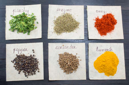Various spices  on recycled papers with labels placed  on a dark wooden table