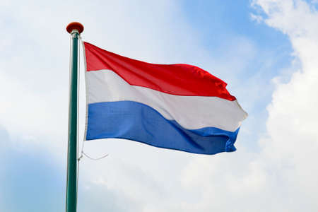 Dutch flag waving in the air on a partly cloudy dayの写真素材
