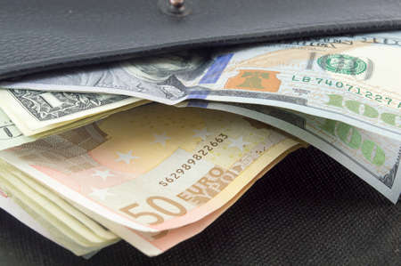Various euro and dollar bills in a black wallet