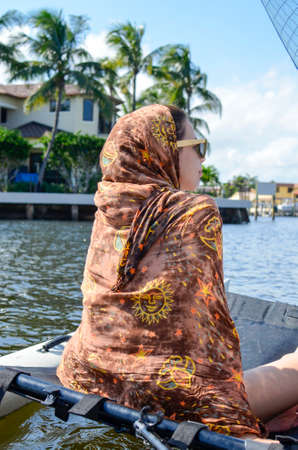 Beautiful girl covered with hippie scarf sails the sea surrounded by palm trees