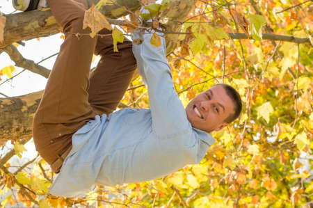 Smiling handsome man hanging from the tree in the parkの写真素材