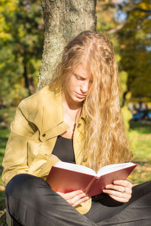 Blonde girl reading a red book in a park on a sunny dayの写真素材