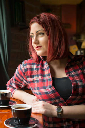 redhead girl in a plaid shirt at a coffee shop looking at the windowの写真素材