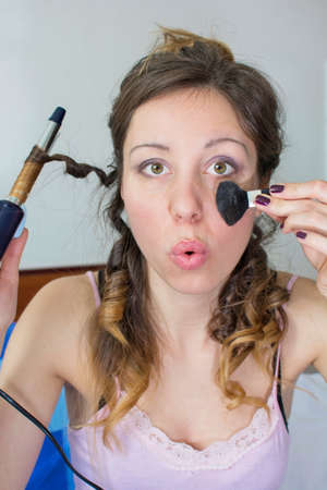 Girl straightening her hair and putting on makeup indoorsの写真素材