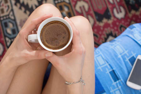 Girl having coffee in bed with her smartphone