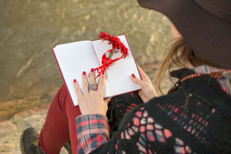 Romantic girl with a book by the river bank holding red flower