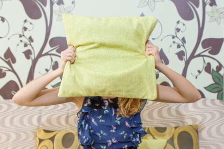 girl hiding behind a green pillow sitting in the living room sofaの写真素材