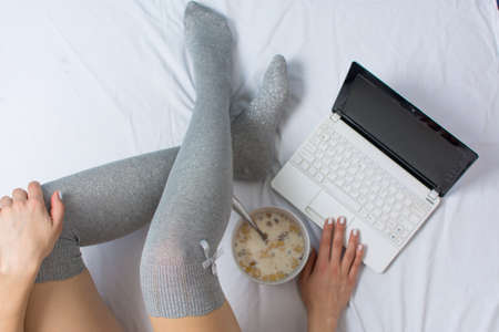 Girl working and eating cereals for breakfast in bedの写真素材