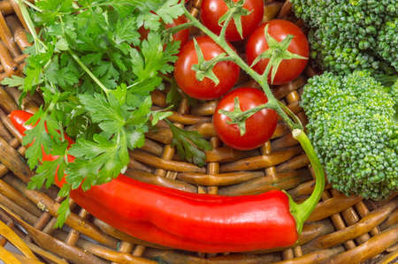 Cherry tomatoes with parsley, broccoli and red pepper on a wooden plateの写真素材