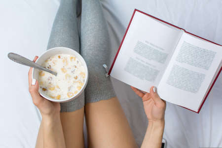 Woman eating cereals and reading in bed top viewの写真素材
