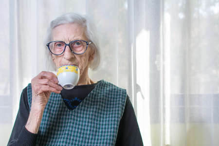 Ninety years old womand having cup of coffee indoorsの写真素材