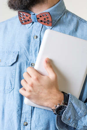 Bearded man with a wooden bow tie holding a white tablet