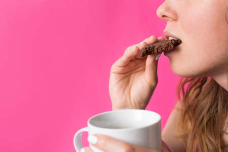 Woman eating cookie with cup of coffee in her handsの写真素材