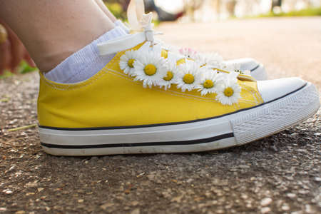 Yellow sneakers decorated with daisies in the parkの写真素材