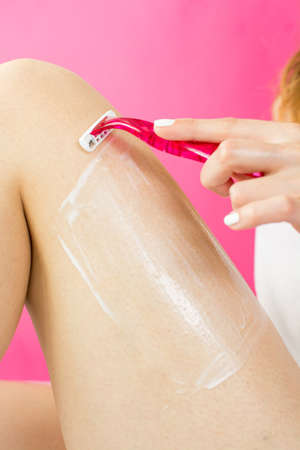 woman shaving her leg with red shaverの写真素材