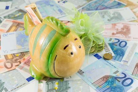 Toy fish piggy bank on top of euro billsの写真素材
