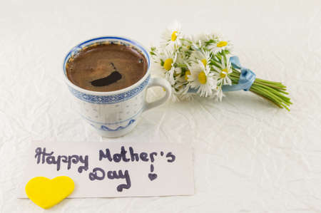 Happy mothers day note with cup of coffee and chamomile bouquet