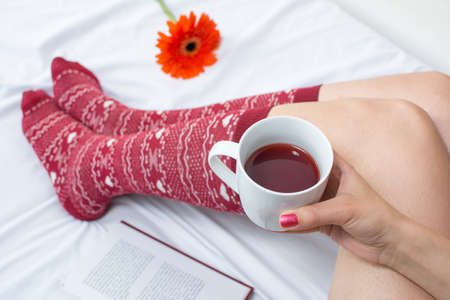 Woman holding a cup of tea in bed and reading a book
