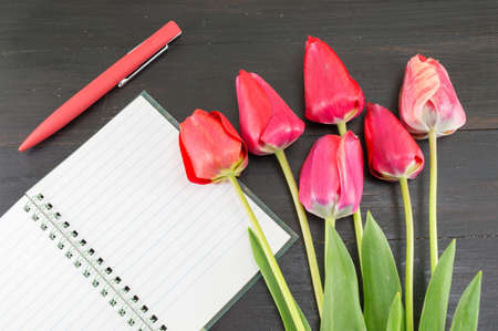 Red tulips and a notebbok on a dark wooden tableの写真素材
