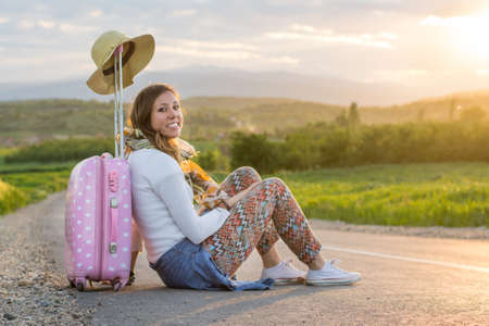 Lonely girl sitting on the road next to her suitcaseの写真素材