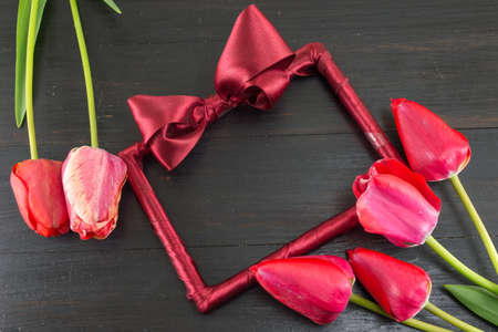 Red tulips and a decorated photo frame on a dark wooden tableの写真素材