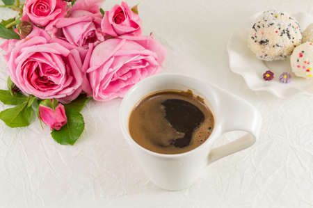 Pink roses and a coffee cup on white silk textileの写真素材