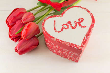 Red tulips and a present box on white wooden boardの写真素材
